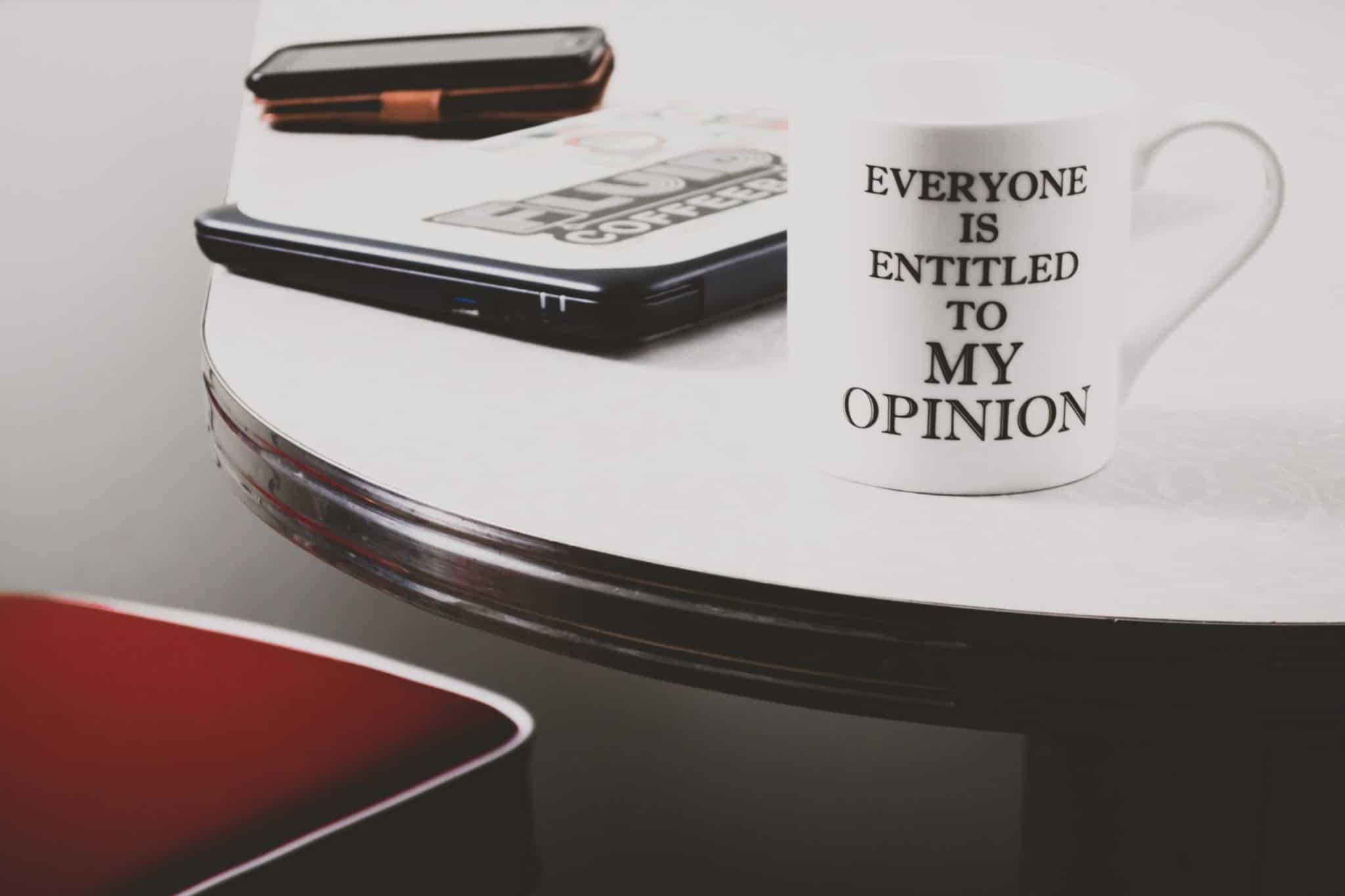 White mug on a table with the inscription "Everyone is entitled to my opinion"