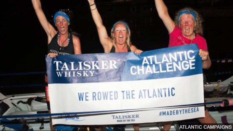 Picture of three women on a rowing boat: Bird Watts, Claire Allinson and Mo O'Brien celebrating the completion of their Atlantic crossing by rowboat